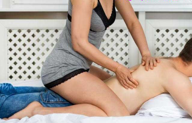 a woman in mini dress massaging client's back by sitting on his back